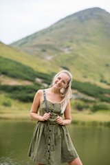 A young woman in the mountains is smiling and happy. Blonde girl in a green dress in the mountains
