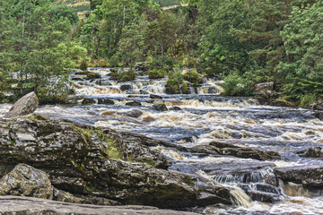 Fototapeta na wymiar The Falls of Dochart, spectacular waterfalls and white water rapids on the River Dochart as it flows through dense woodland in the village of Killin, near Loch Tay in the Scottish Highlands.