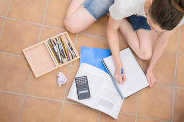 Woman on the floor taking notes together with pencil case and calculator