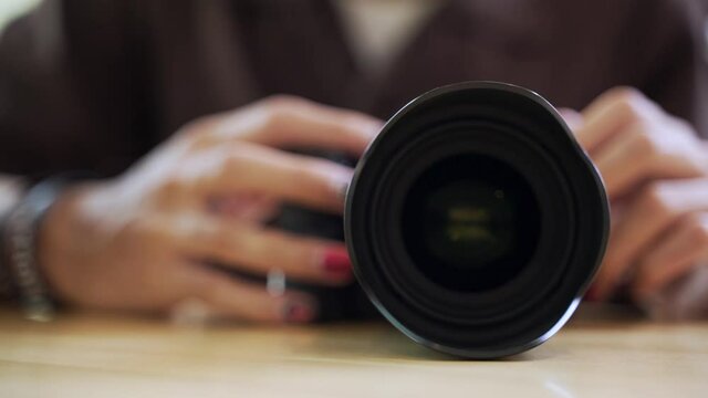 Hand adjusting modern professional camera for photography on wooden desk
