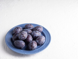 Plum fruit on a blue plate on a white background.