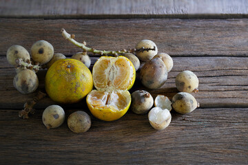 Oranges and Longkong (Thai fruit) rotten and withered fruits with fungus and fruit fly on old wooden table which has black background