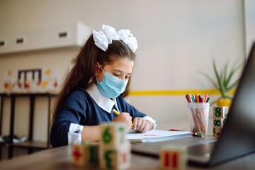 School girl in medical mask using laptop computer studying through online e-learning system. Remote lessons. Distance learning.  Covid-2019.
