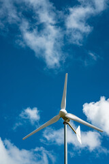 A white wind power turbine with blue sky.