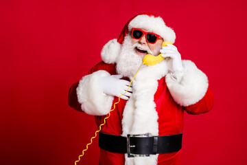 Photo of pensioner old man grey beard hold wired telephone talk snow maiden receive compliment hand chest wear x-mas santa costume gloves coat sunglass cap isolated red color background