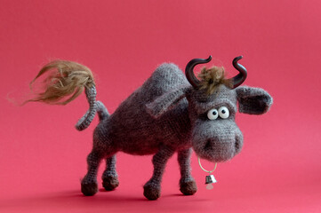 Toy bull. The bull is a symbol of the New year 2021. Knitted brown toy bull on a red background. Copy Space, close-up, selective focus.