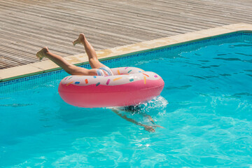 cute young girl playing in the pool with her inflatable donut
