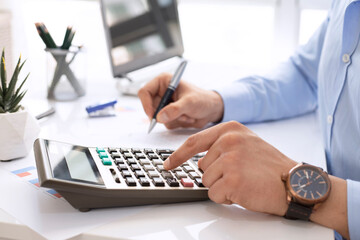 Close up of businessman or accountant hand holding pen working on calculator to calculate financial data report, accounting document and laptop in office, business concept