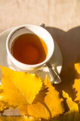 White cup with tea and yellow autumn leaves on white table