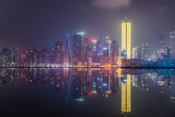 Night view of the skyline of downtown Chongqing on a cloudy day, with reflection in front.