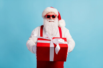 Portrait of his he nice attractive cheerful white-haired Santa father holding in hands big red bow ribbon gift December Eve Noel isolated bright vivid shine vibrant blue color background