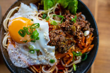A bowl of spice beef noodles with a pan fried egg.