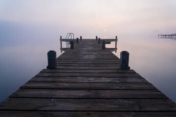 Jetty during a foggy and tranquil sunrise at a lake.
