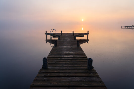 A jetty in a lake during a tranquil, foggy dawn. © sanderstock