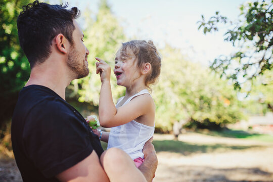 Young dad playing with daughter in his arms outside in summer