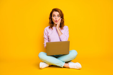 Full length photo of impressed funny woman sit legs crossed work laptop read unbelievable news touch hands cheeks scream wow omg wear stylish jumper isolated over shine color background