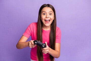 Photo portrait of young schoolgirl playing video games holding gamepad with both hands screaming laughing wearing pink casual t-shirt isolated on purple color background