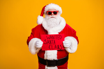 Portrait of his he nice attractive bad Santa disguise hardened criminal holding in hands red board wanted search seeking isolated over bright vivid shine vibrant yellow color background