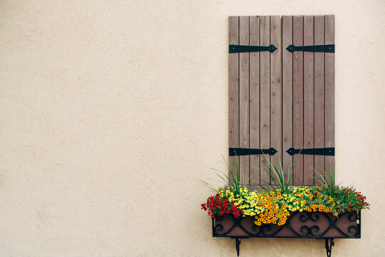 Closed Window With Colorful Flower Boxes and Wooden Shutters in a Stucco Wall