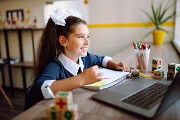 Beautiful school girl sitting at the table, draws and studying homework. School girl using laptop computer studying through online e-learning system.  Distance learning.  Covid-2019.