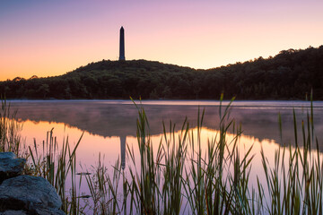 Tall obelisk monument on a mountain reflecting in still water at sunrise. High Point State Park, New Jersey - obrazy, fototapety, plakaty