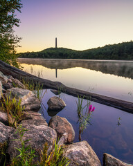 Tall obelisk monument on a mountain reflecting in still water at sunrise. High Point State Park,...