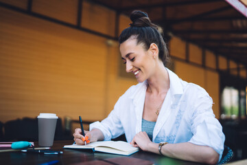Happy female freelancer writing article in notebook