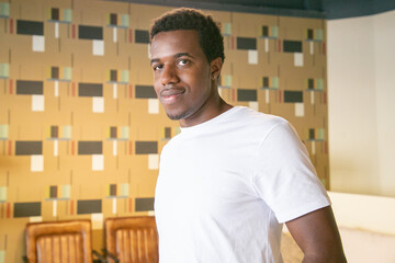 Positive handsome African American guy in whit t-shirt standing and posing in co-working or coffee...