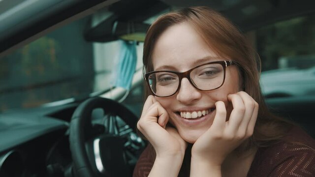 Close up, Face expression of young caucasian woman sitting on the driver seat. Face mask hanging on the mirror. High quality 4k footage
