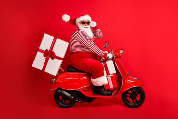 Full length profile photo of grandfather grey beard ride retro moped deliver box wear santa claus x-mas costume suspenders sunglass striped shirt cap boots isolated red color background