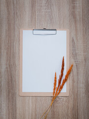 Blank clipboard with dry flowers decoration on wooden desk background.