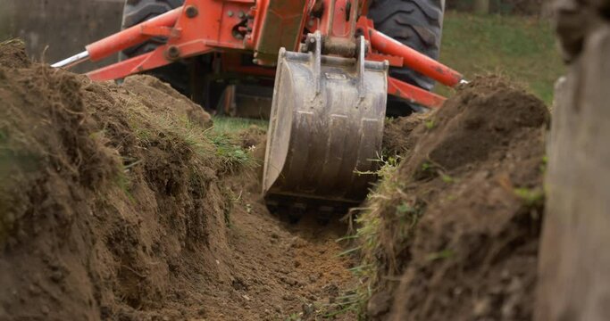 A Low Angle View Of A Small Backhoe Digging A Drainage Ditch. With Audio.	