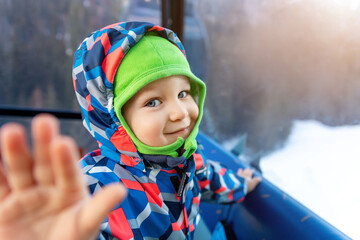 Cute adorable happy caucasian smiling toddler kid boy enjoy ascent sitting inside ski lift gondola cable car and giving high five gesture to parent mom or dad. Winter travel with children concept