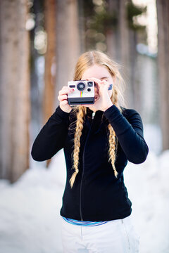 Teenage girl takes a polaroid photo on a snowy morning in winter