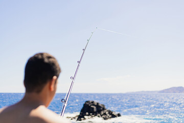 Young dark short-haired man of Maghreb origin fishing on his back, with the fishing rod raised in the foreground.