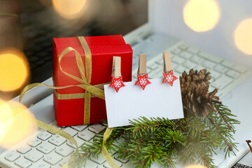Red gift box on the laptop.White paper business card with wooden clothespins on the background of a green branch of a Christmas tree with cones.Christmas shopping sale.Happy new year.Copy space.Text