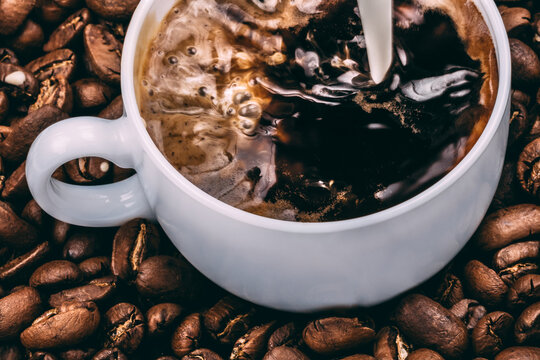 Pouring milk to coffee cup standing on roasted coffee beans background