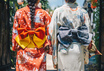 Rear view of two Japanese women wearing Yukata dress while walking in town. A Japanese yukata is a lightweight form of kimono, which is worn casually during the summer.