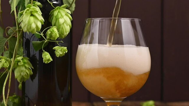 Beer. Cold Craft light Beer in a glass with water drops. Pint of Beer close up on a wooden background. Beer is pouring from the bottle. Border design. High quality 4k footage