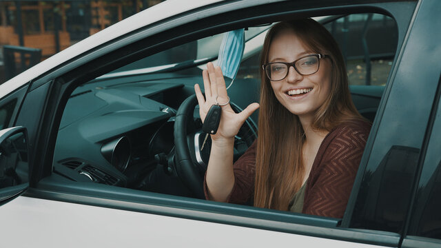 Happy face expression of young caucasian woman sitting on the driver seat and waving with car keys. High quality photo