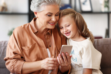 Happy grandmother sharing media on smartphone with granddaughter.