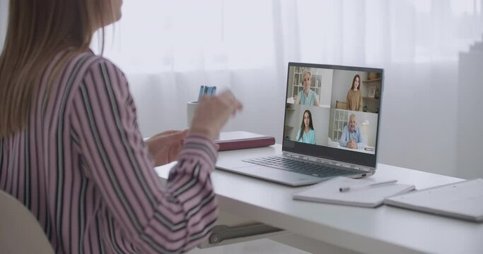 Back view of female employee speak talk on video call with diverse multiracial colleagues on online briefing, woman worker have Webcam group conference with coworkers on modern laptop at home