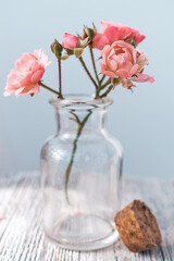 Small pink roses in a glass vase on the white wooden table.Selective focus
