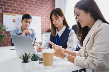 Asian group of business people working in office. Close-up of a beautiful woman using a phone on the table.