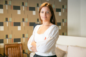 Confident beautiful young business woman standing with arms folded and posing in co-working or coffee shop interior, looking at camera. Medium shot. Professional portrait concept
