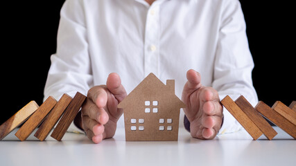 a businessman or a butler using his hand to protect the house from the falling of a wooden...