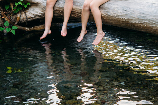two girls on a fallen log over a creek dangling bare feet in water