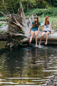 two girls on a log dangling feet in creek