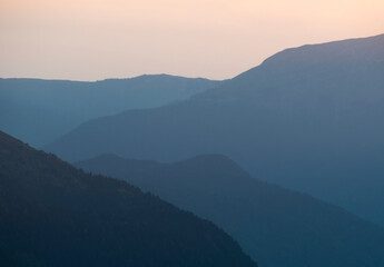 Fototapeta premium Silhouette of layered mountains ridge at sunset. Blue gradient background