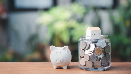 Saving money for house with coins,house and piggy bank model on wood table nature green background